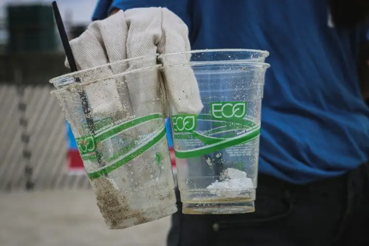 Eine Person mit weißer Handschih hält zwei leere, durchsichtige Plastikbecher.